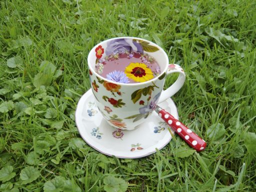 Bunte Tasse mit Blumen und einem Löffel auf grünem Gras.
