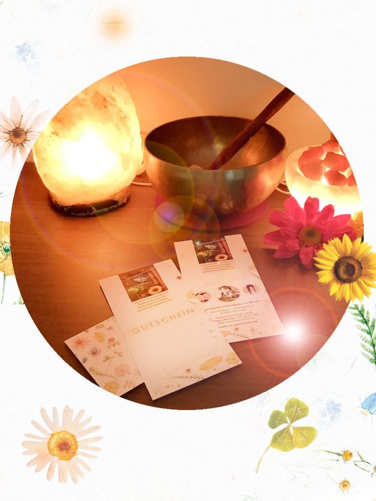 Klangschale, Kerzen und blühende Karten auf einem Tisch in sanftem Licht.